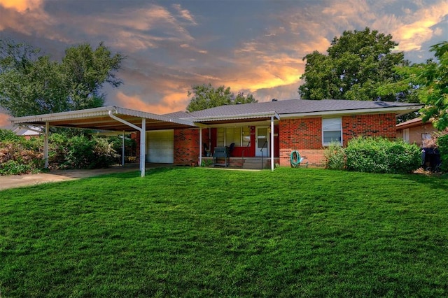 back of property with a carport, an attached garage, a lawn, and brick siding