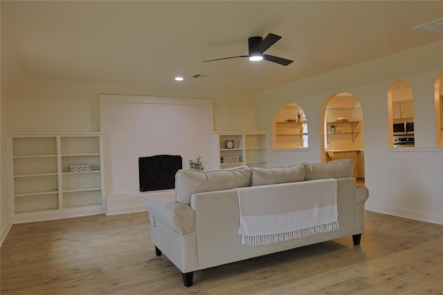 living area with arched walkways, ceiling fan, light wood-style flooring, and baseboards