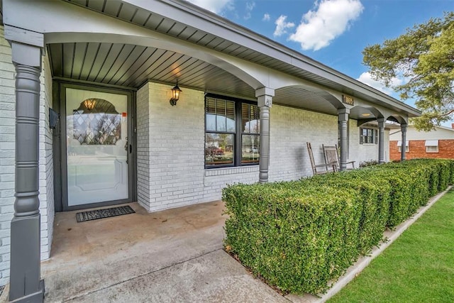 entrance to property featuring a porch and brick siding