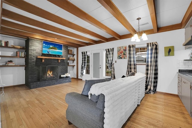 living area with light wood finished floors, a brick fireplace, beam ceiling, and an inviting chandelier