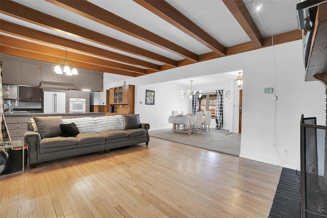 living area with baseboards, beam ceiling, light wood-style flooring, and a notable chandelier