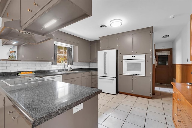 kitchen with white appliances, visible vents, dark countertops, a peninsula, and a sink