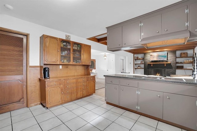 kitchen with glass insert cabinets, a brick fireplace, gray cabinetry, and light tile patterned floors