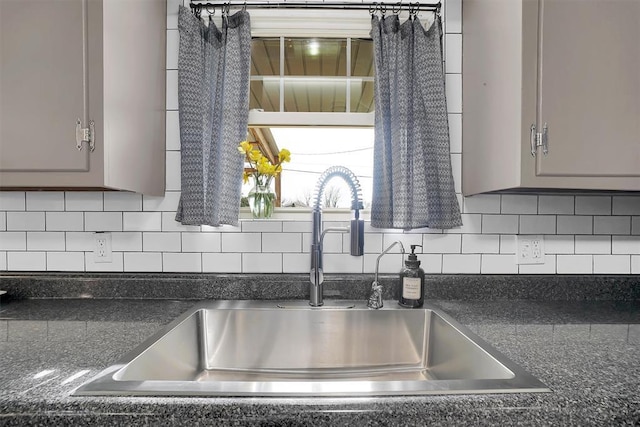 kitchen with dark countertops, decorative backsplash, a sink, and gray cabinetry