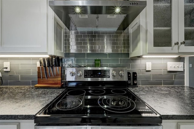 kitchen with electric stove, tasteful backsplash, dark countertops, white cabinets, and wall chimney range hood