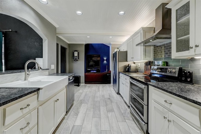 kitchen with stainless steel appliances, wood finish floors, a sink, wall chimney range hood, and decorative backsplash