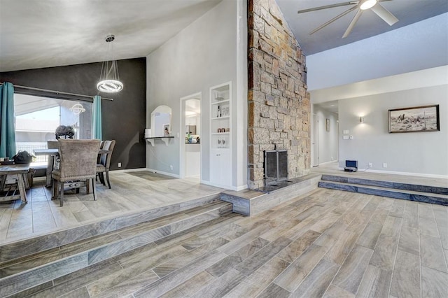 interior space featuring high vaulted ceiling, a fireplace, a ceiling fan, baseboards, and wood tiled floor