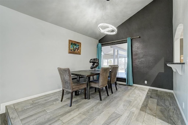 dining space with baseboards, high vaulted ceiling, an inviting chandelier, and light wood-style floors