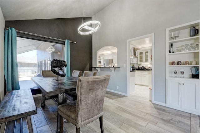 dining space with light wood-type flooring, baseboards, a high ceiling, and arched walkways