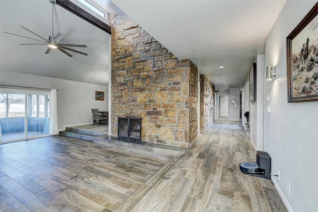 unfurnished living room featuring ceiling fan, a stone fireplace, baseboards, and wood finished floors