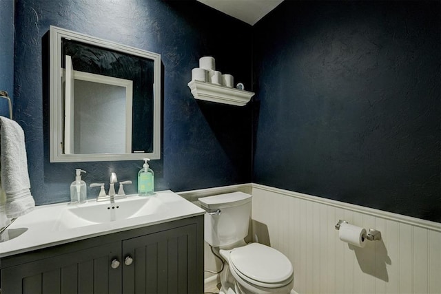 bathroom featuring a textured wall, wainscoting, vanity, and toilet