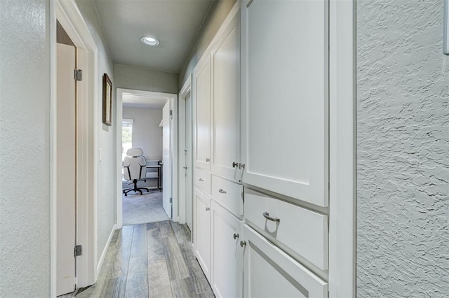 hall with a textured wall, light wood finished floors, and baseboards