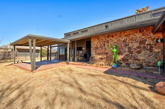 back of house featuring stone siding, a patio, and fence