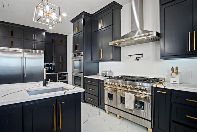 kitchen with premium appliances, marble finish floor, a sink, dark cabinetry, and wall chimney exhaust hood