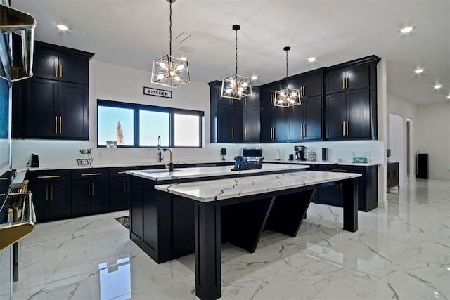 kitchen with marble finish floor, a center island with sink, dark cabinetry, and a sink