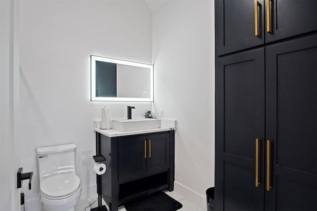 half bathroom with marble finish floor, baseboards, vanity, and toilet