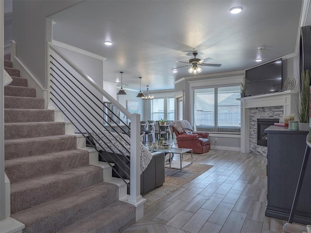 stairs with a fireplace, ceiling fan with notable chandelier, crown molding, and wood finished floors