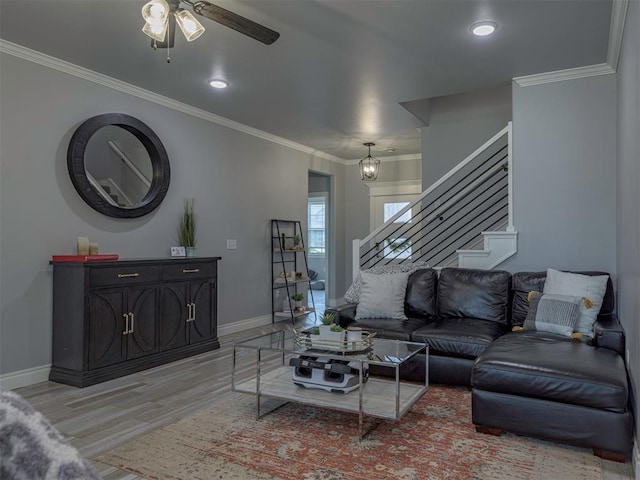 living room featuring light wood-style flooring, a ceiling fan, baseboards, stairs, and crown molding