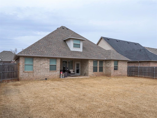 rear view of house with a patio area, roof with shingles, a lawn, and brick siding