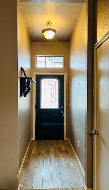 doorway to outside featuring light wood-style flooring, a textured ceiling, and baseboards