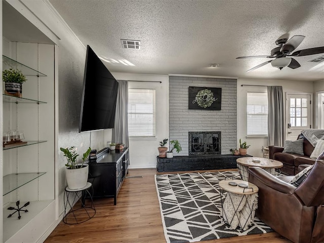 living room with a fireplace, light wood-style floors, visible vents, and a ceiling fan