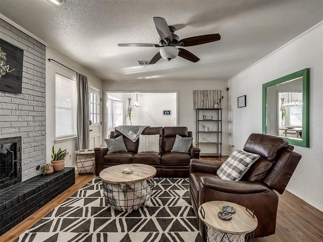 living area featuring wood finished floors, visible vents, ceiling fan, a textured ceiling, and a brick fireplace