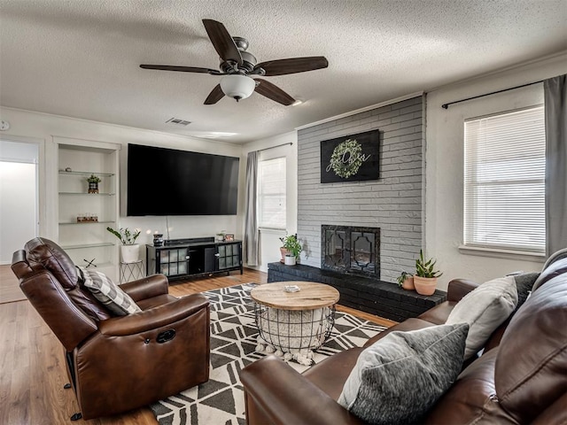 living area with built in features, a ceiling fan, wood finished floors, a textured ceiling, and a brick fireplace