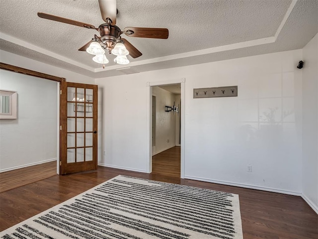 empty room with a tray ceiling, wood finished floors, and a textured ceiling