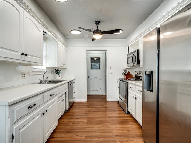 kitchen with a ceiling fan, wood finished floors, a sink, stainless steel appliances, and white cabinets