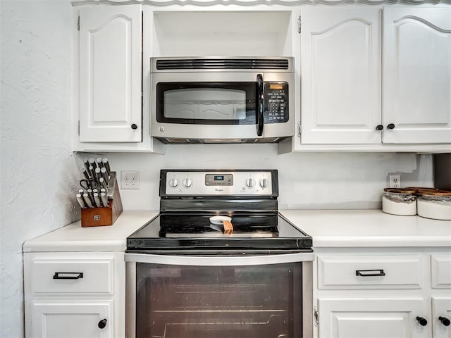 kitchen with a textured wall, appliances with stainless steel finishes, white cabinets, and light countertops