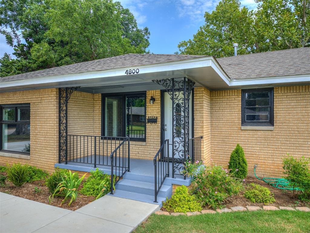 property entrance featuring a porch, roof with shingles, and brick siding