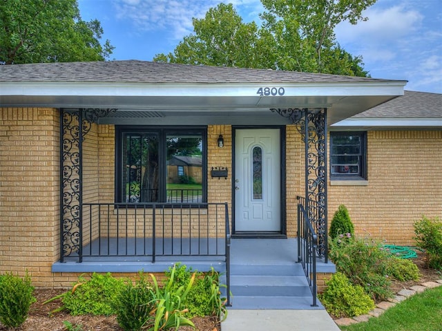 property entrance featuring a shingled roof, a porch, and brick siding