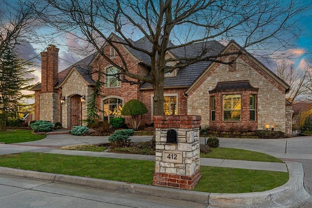 view of front of property with brick siding, a yard, stone siding, driveway, and a chimney