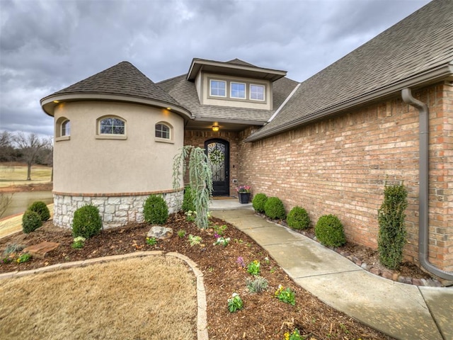 property entrance with a shingled roof and brick siding