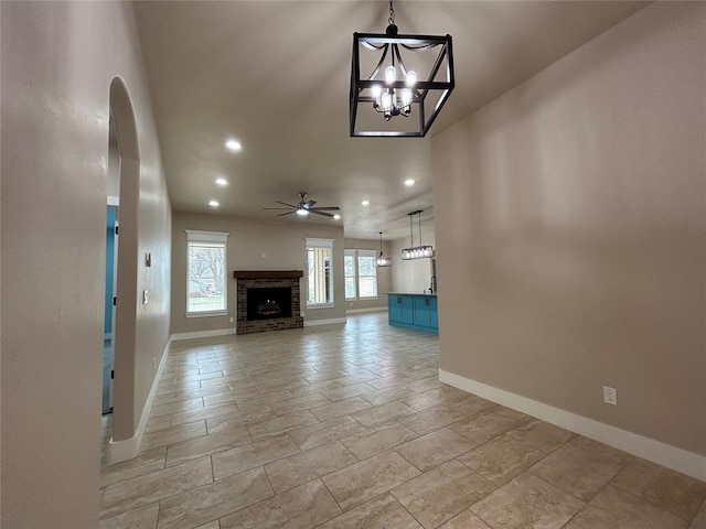 unfurnished living room featuring recessed lighting, baseboards, arched walkways, a fireplace, and ceiling fan with notable chandelier