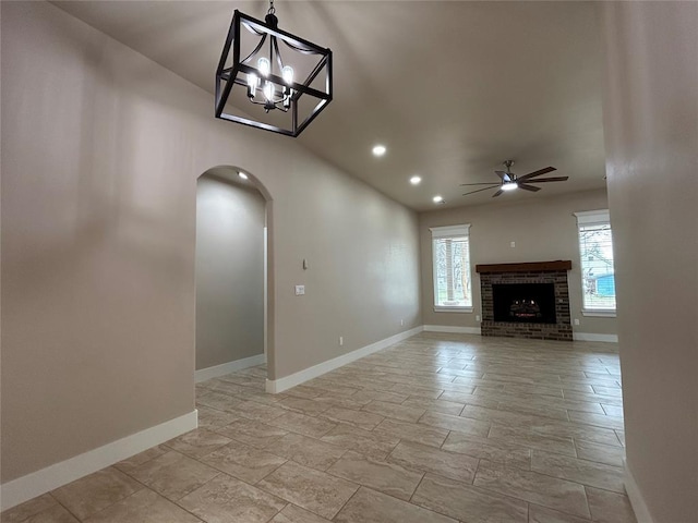 unfurnished living room featuring a brick fireplace, baseboards, and ceiling fan with notable chandelier