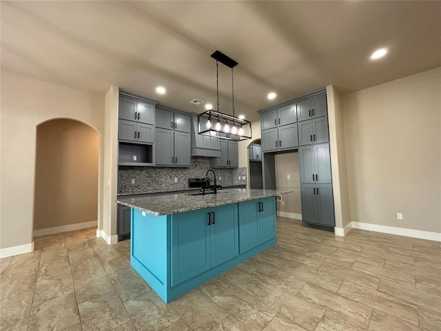 kitchen featuring dark stone countertops, arched walkways, gray cabinets, and decorative backsplash