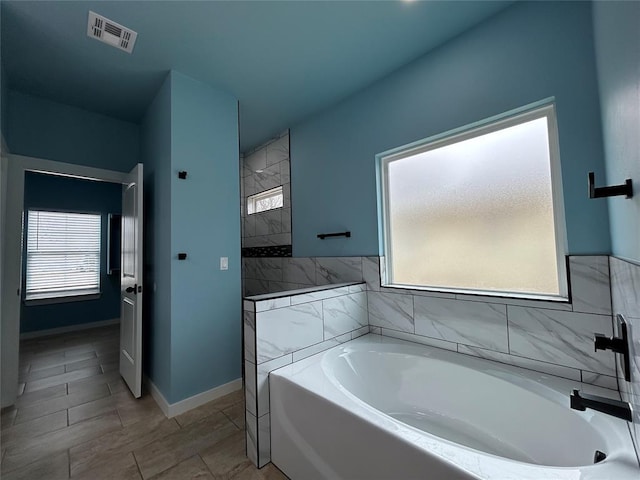 bathroom featuring a bath, a wealth of natural light, a walk in shower, and visible vents