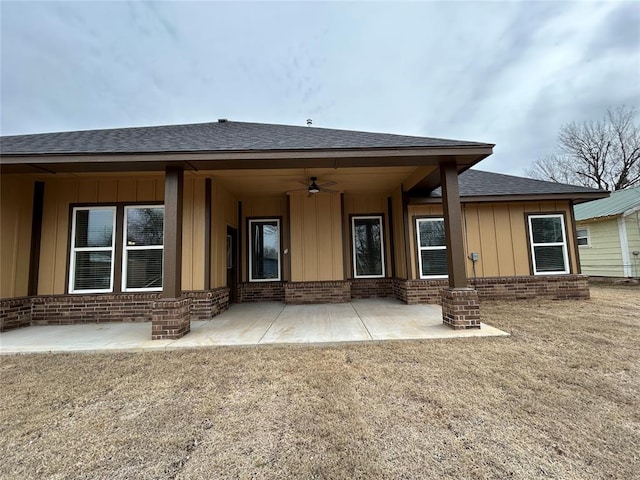 back of house featuring a patio area, roof with shingles, board and batten siding, and brick siding