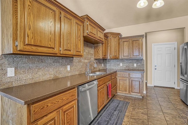 kitchen with brown cabinetry, dark countertops, appliances with stainless steel finishes, a sink, and backsplash