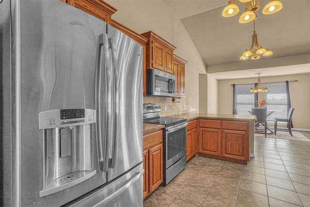 kitchen featuring brown cabinetry, appliances with stainless steel finishes, a peninsula, vaulted ceiling, and a notable chandelier