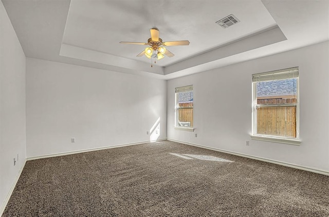 empty room featuring visible vents, a raised ceiling, baseboards, ceiling fan, and carpet