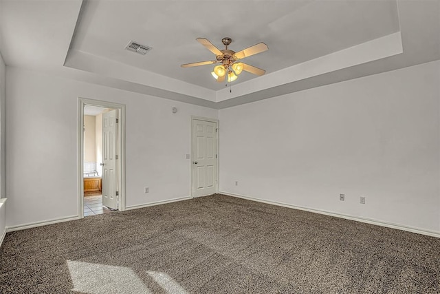 carpeted spare room with visible vents, a tray ceiling, ceiling fan, and baseboards