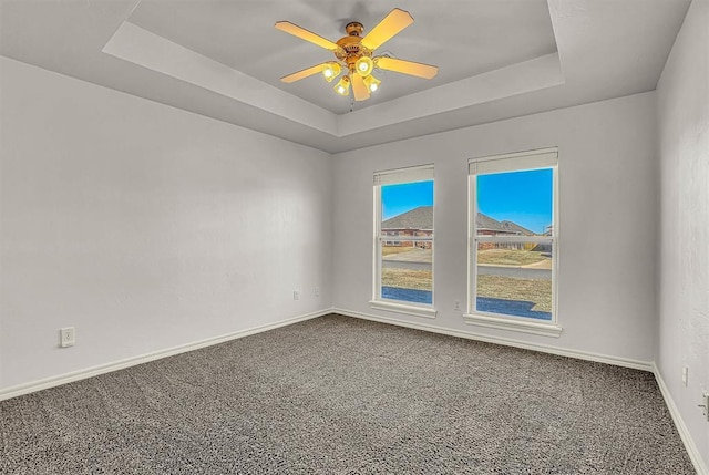 spare room featuring carpet floors, a raised ceiling, and baseboards