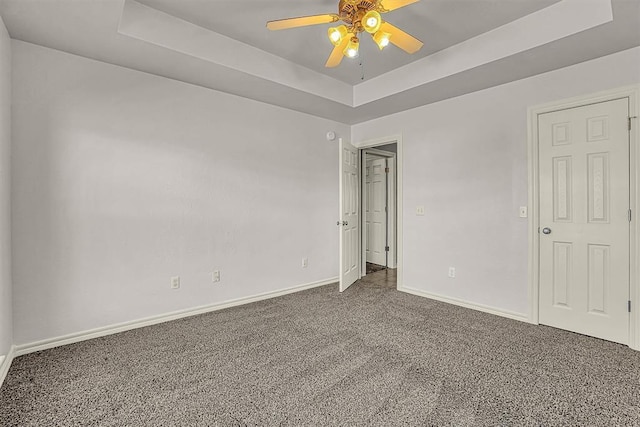 unfurnished room featuring a tray ceiling, carpet flooring, ceiling fan, and baseboards