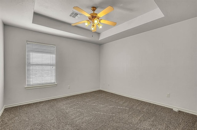 carpeted empty room with visible vents, a tray ceiling, and baseboards