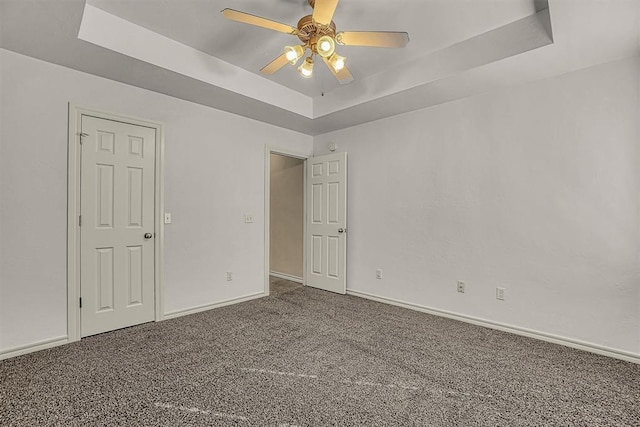 unfurnished bedroom featuring carpet flooring, a raised ceiling, a ceiling fan, and baseboards