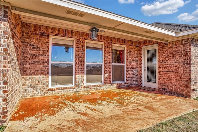 view of exterior entry featuring a patio area, brick siding, and visible vents