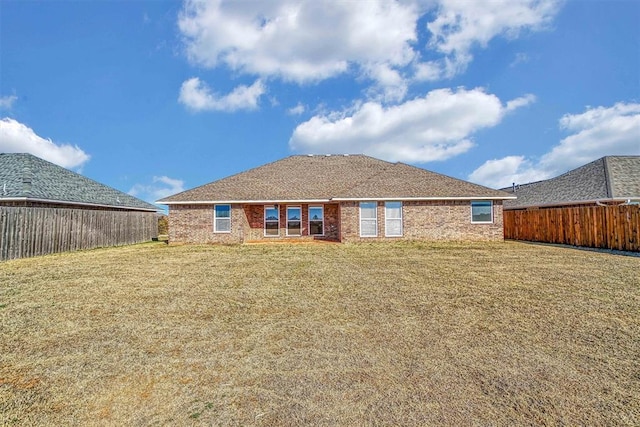 back of property featuring brick siding, a lawn, and fence