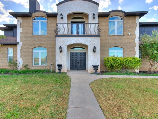 view of front of home featuring a front yard, french doors, brick siding, and a balcony